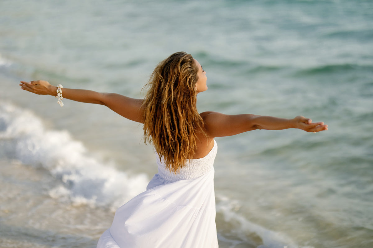 Luxvivendi Longevity – woman in a white dress with arms outstretched by the sea
